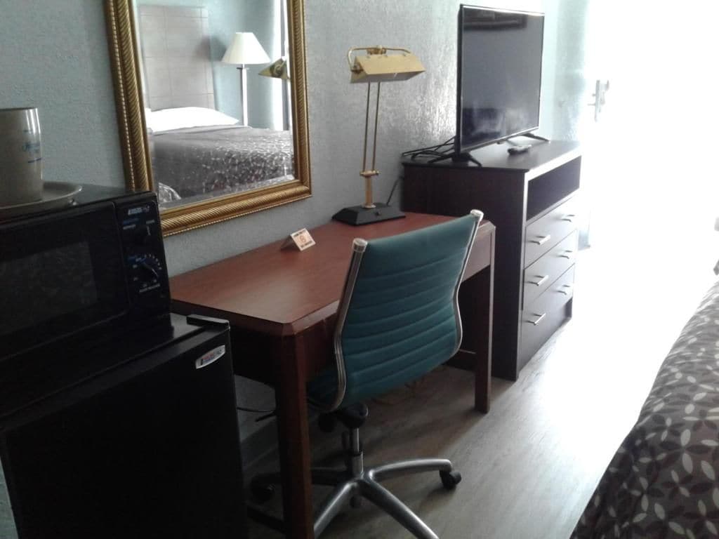 A hotel room with a desk, chair, television, and a bed.