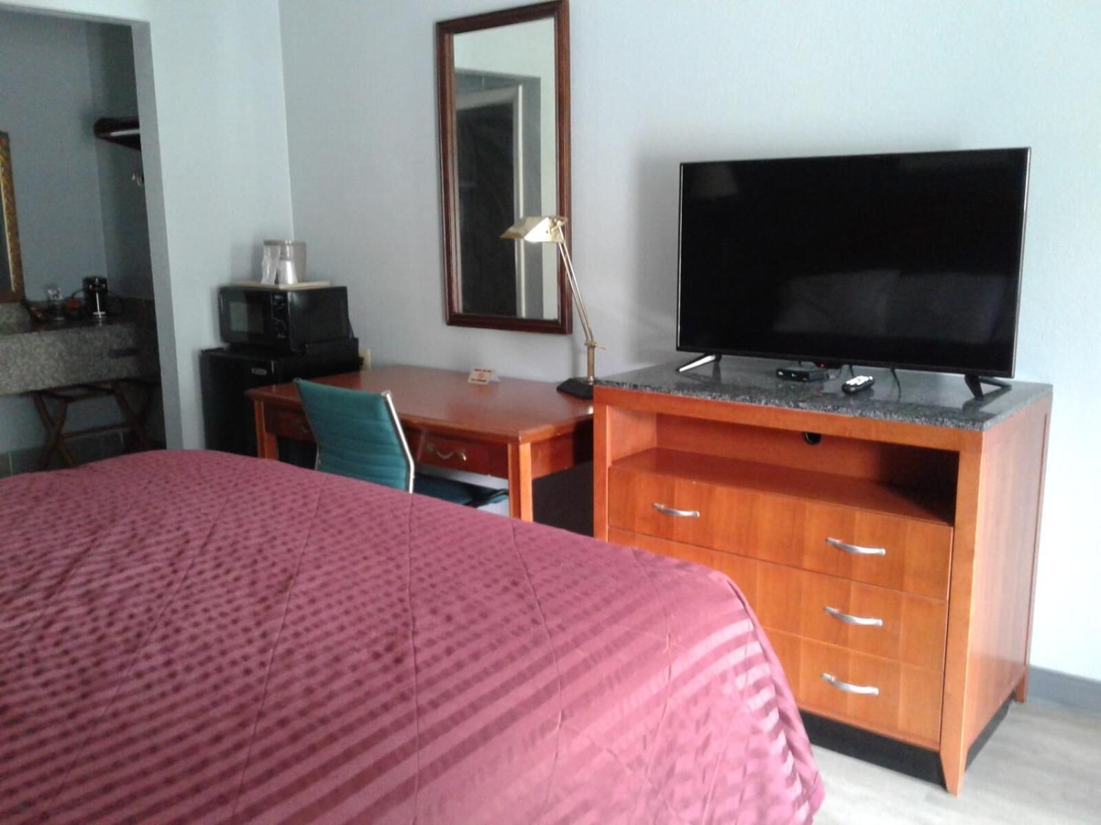 A hotel room with a bed, a desk with a television, a chair, and a desk lamp.