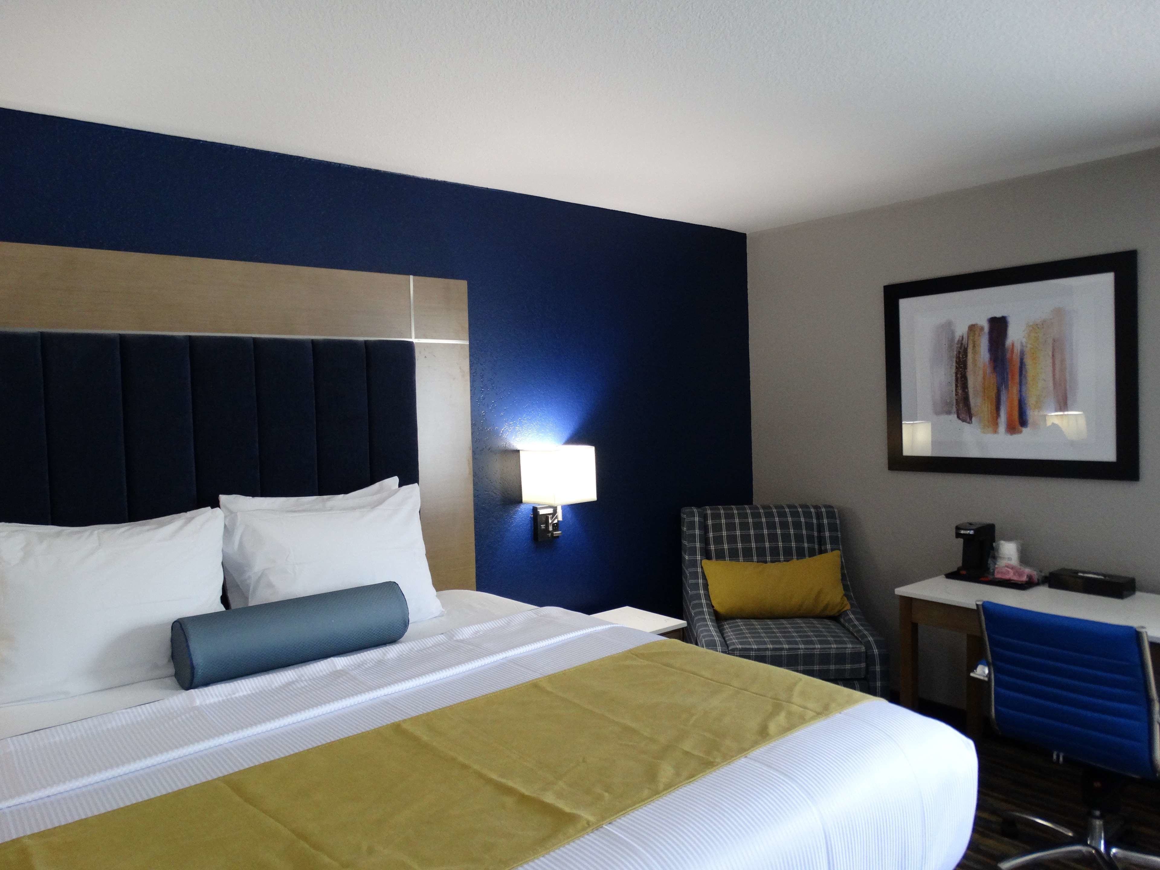 A hotel room with a bed, a desk, a chair, and a wall-mounted lamp.