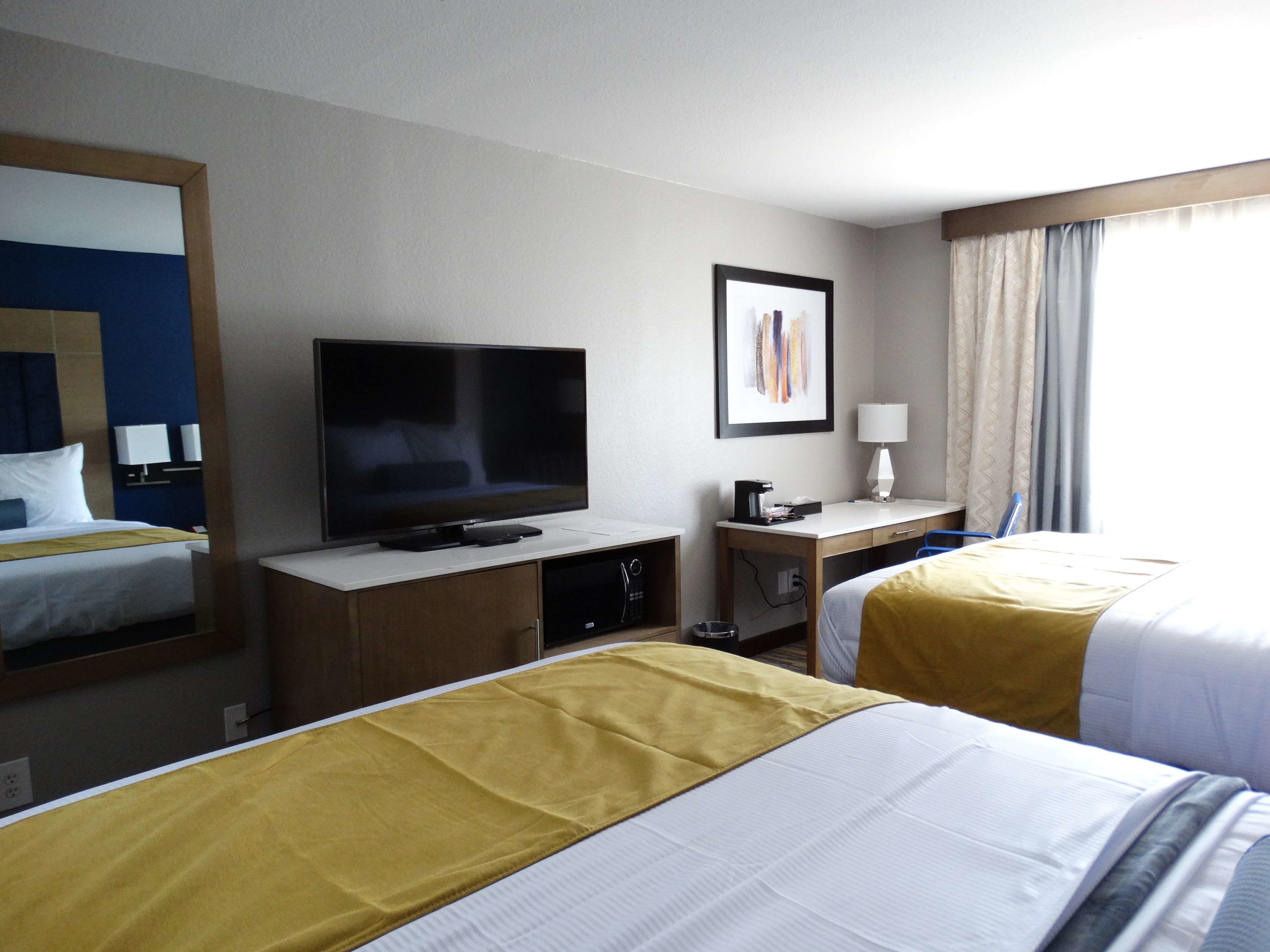 Een hotelkamer met een bed, een bureau met een televisie, een lamp en een raam met gordijnen.