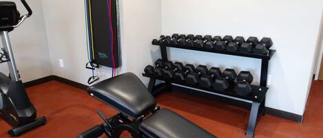 A gym with a bench, dumbbells, and a stationary bike.