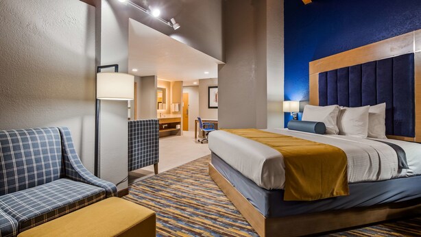 A hotel room with a bed, a chair, a desk, and a bathroom in the background. - Best Western DeWitt (DeWitt)