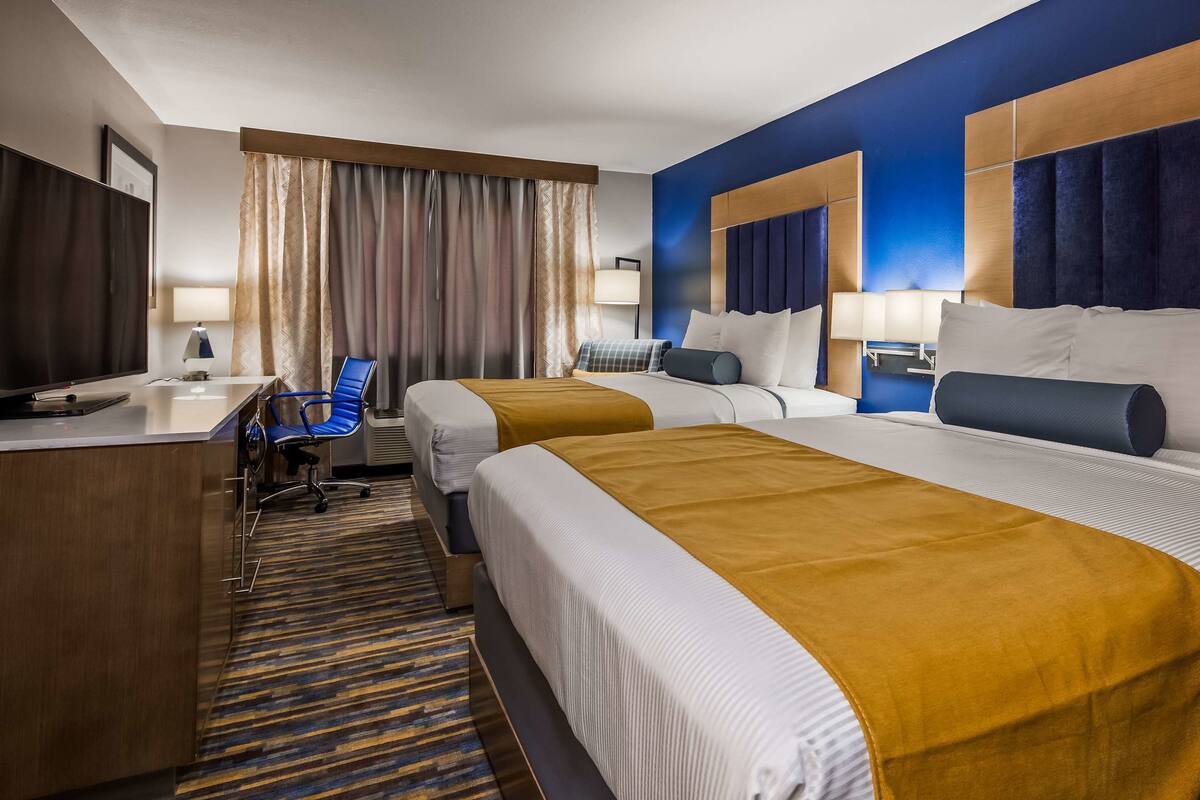 A hotel room with two beds, a desk, a chair, and a TV.