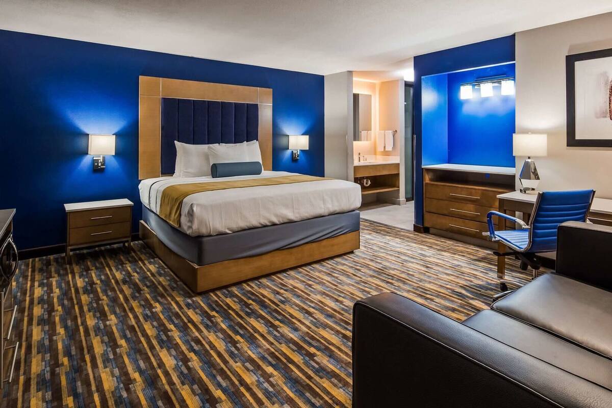 A hotel room with a bed, desk, chair, and a TV.