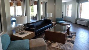 A modern living room with a black sofa, a glass coffee table, and a blue armchair. There is a large window providing natural light and a view of the outdoors. - Best Western DeWitt (DeWitt)