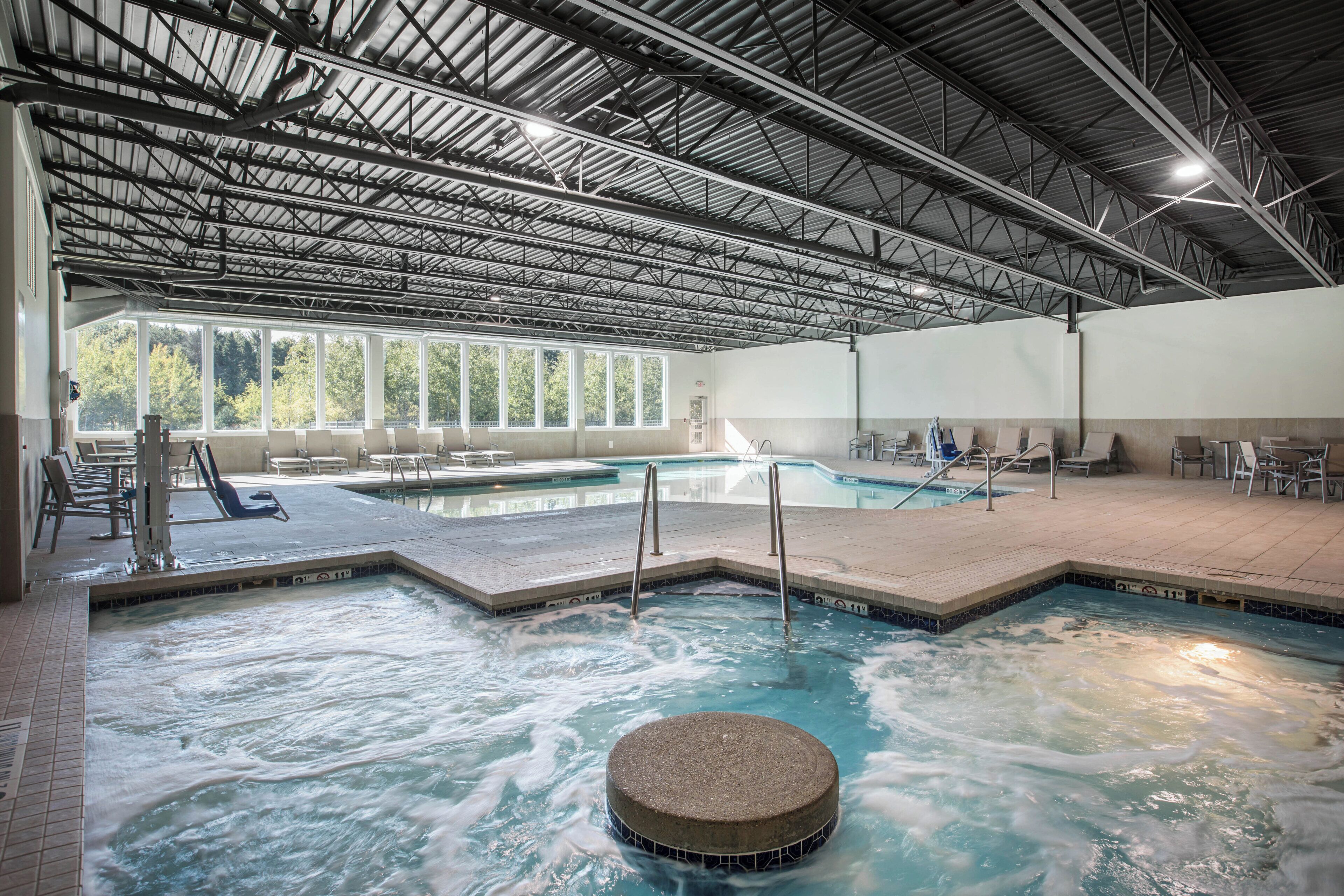 An indoor swimming pool with multiple lanes, a hot tub, and a seating area with chairs and tables.