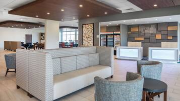 A modern lobby with a sofa, chairs, and a refrigerator.