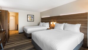 Habitación de hotel con dos camas, cabecero de madera, mesita de noche con lámpara y puerta que da a otra habitación.