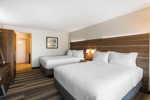 A hotel room with two beds, a wooden headboard, a bedside table with a lamp, and a door leading to another room. - Holiday Inn Express & Suites Ludington by IHG (Ludington)