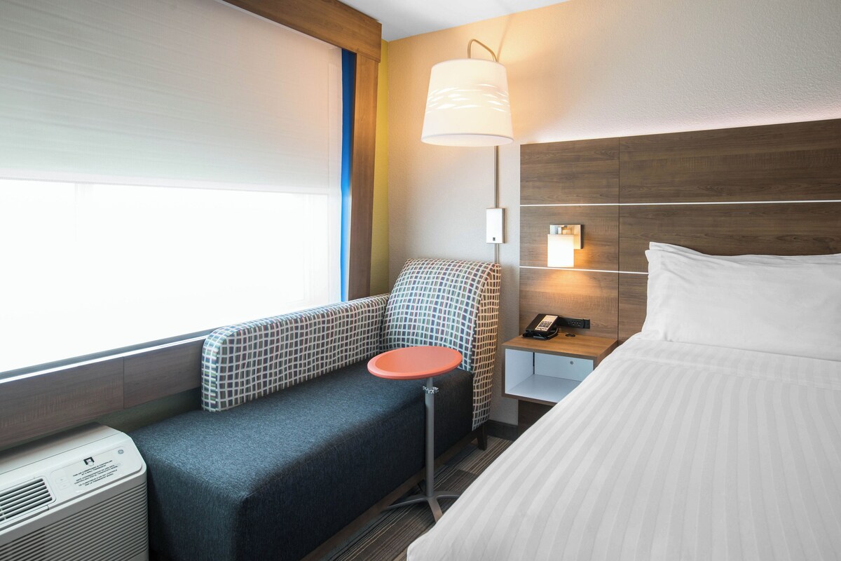 A hotel room with a bed, a small table, a sofa, a lamp, and a heater.