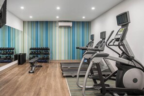 Un gimnasio con cintas de correr, mancuernas y un banco.
