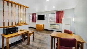 A hotel room with a wooden staircase, a flat-screen TV, a microwave, a wooden table, a chair, and a window with curtains.