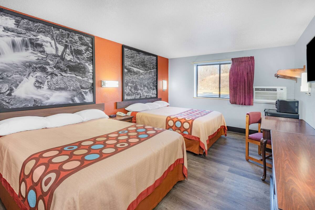 A hotel room with two beds, a desk, a chair, a TV, and a large window.
