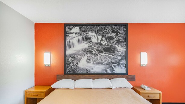 A hotel room with a bed, a large framed waterfall painting on the wall, two bedside tables with lamps, and a patterned bedspread.