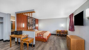 A hotel room with a bed, a desk with a chair, a wooden cabinet, a television, and a window with a curtain.