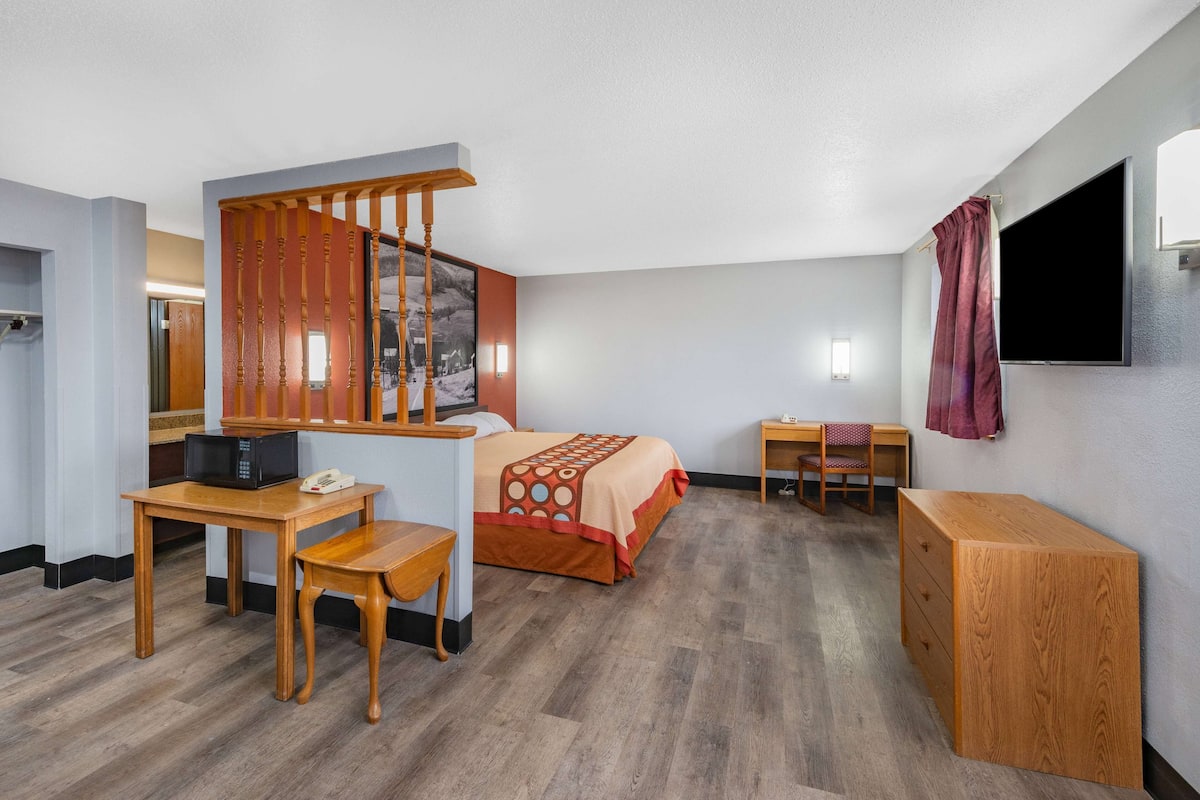 A hotel room with a bed, a desk with a chair, a wooden cabinet, a television, and a window with a curtain.