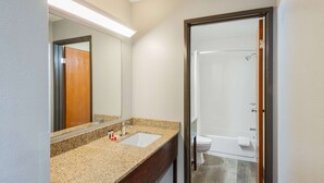 A bathroom with a granite countertop sink, a mirror, and a shower area.
