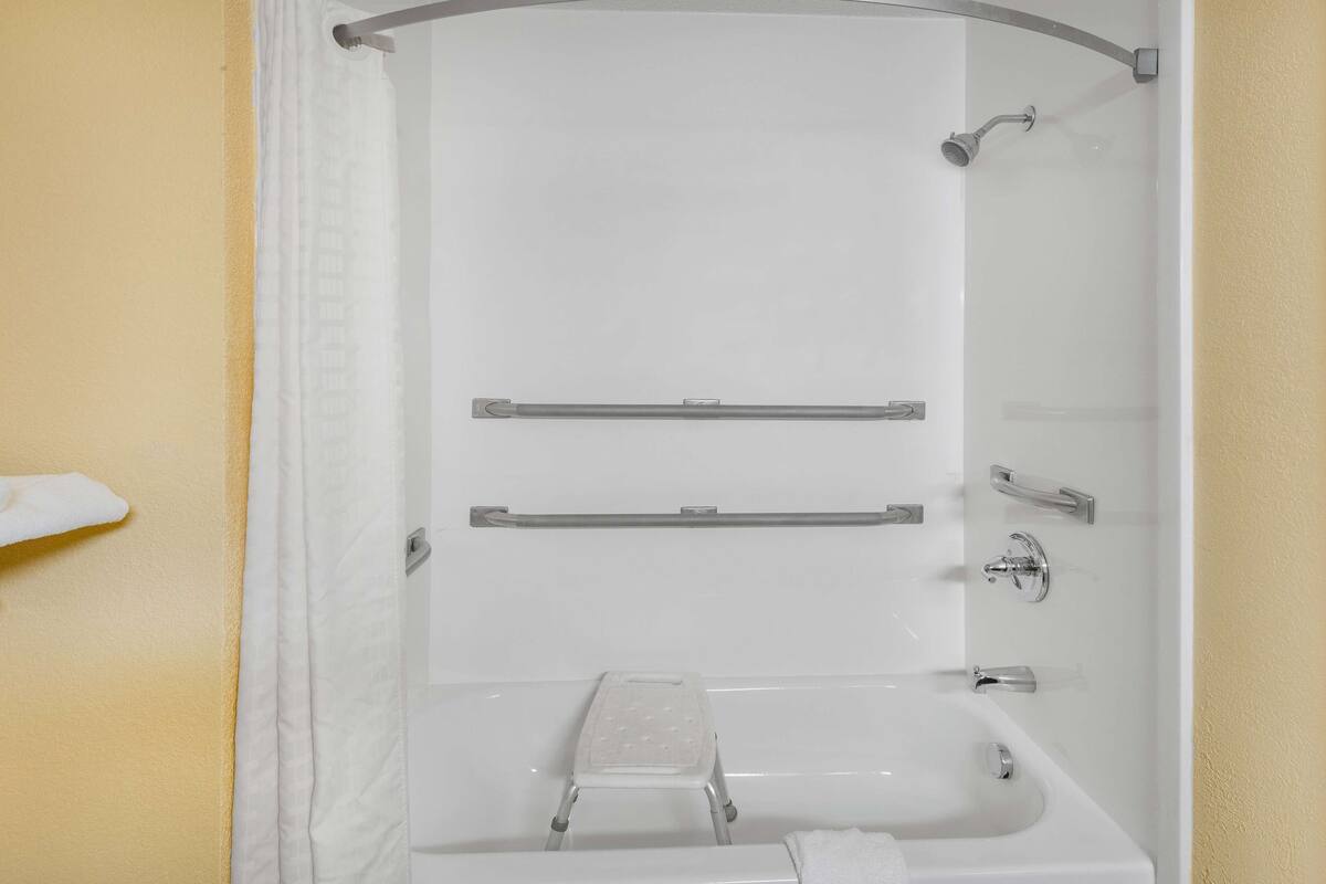 A bathroom with a shower, a bathtub, and a toilet. There are grab bars installed for safety.