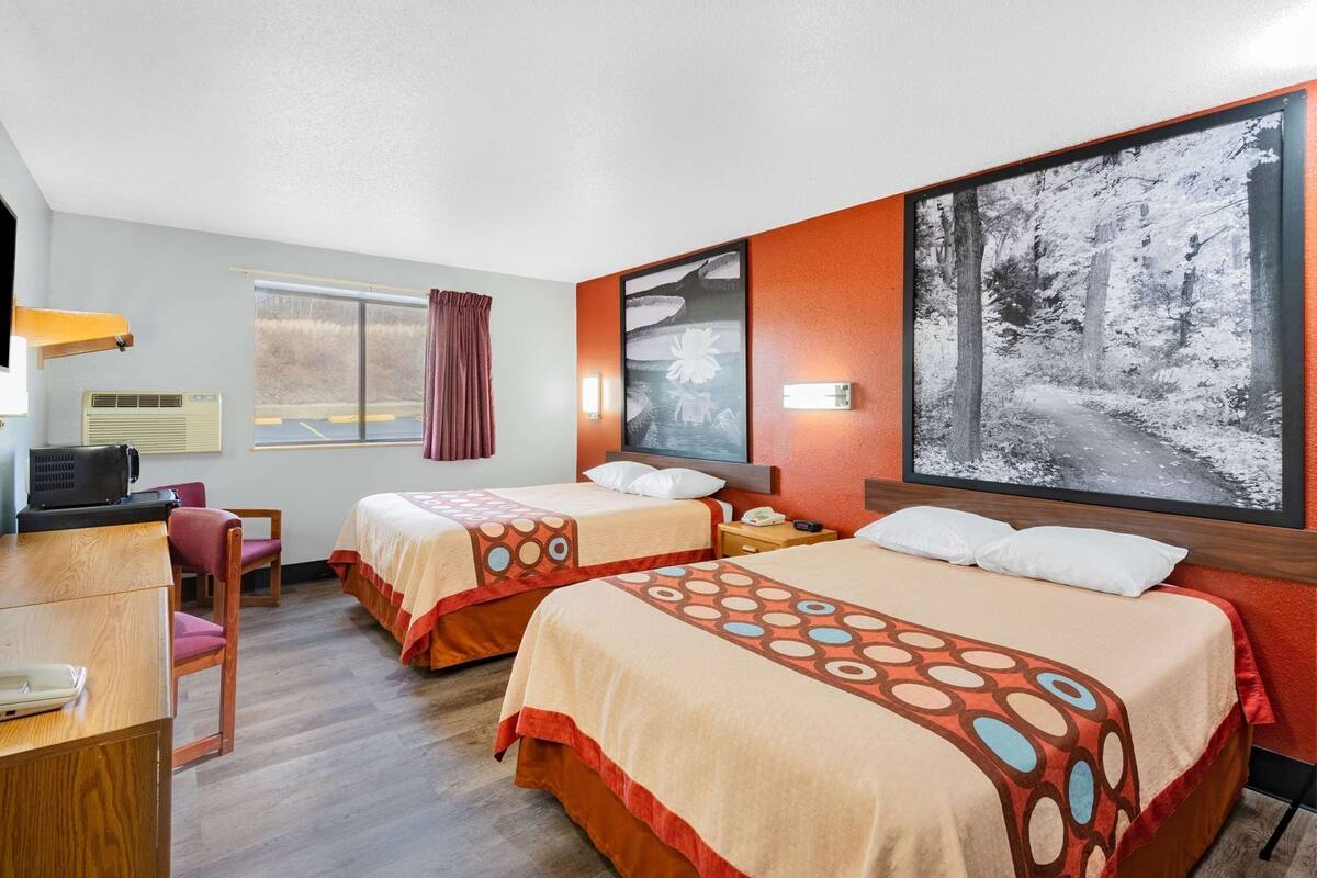 A hotel room with two beds, a desk, a chair, a window with curtains, and a large framed picture on the wall.