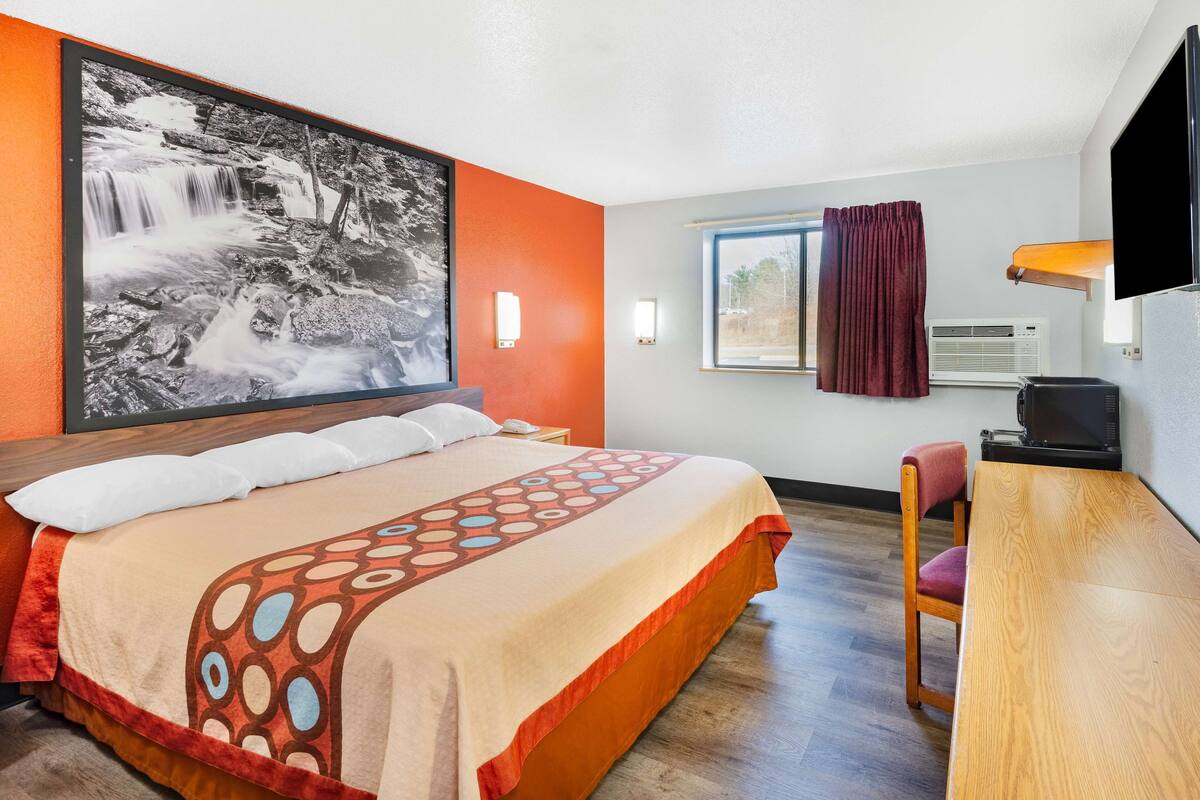 A hotel room with a bed, a desk, a chair, a TV, and a large framed picture of a waterfall.