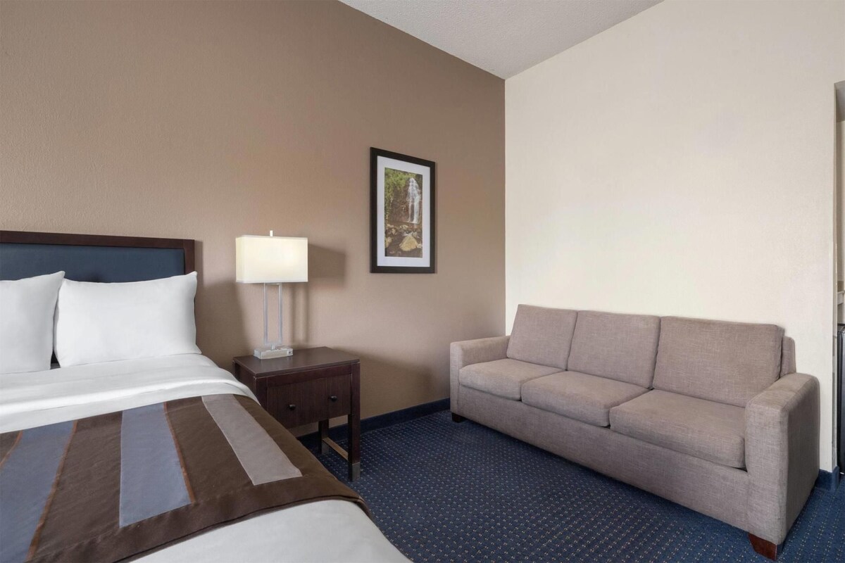 A hotel room with a bed, a nightstand with a lamp, a sofa, and a framed picture on the wall.