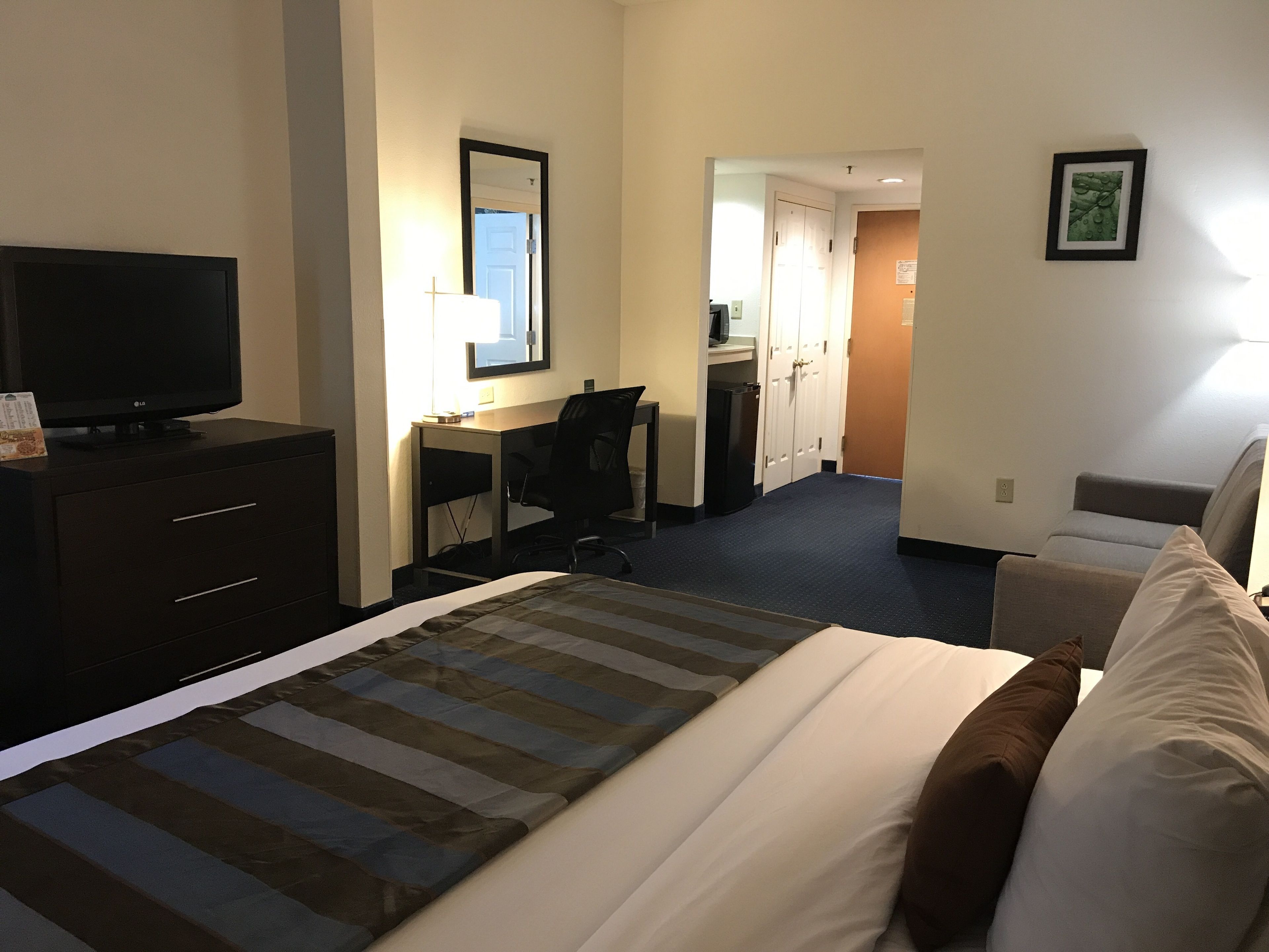 A hotel room with a bed, a desk, a chair, a television, and a bathroom visible through an open door.