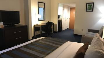 A hotel room with a bed, a desk, a chair, a television, and a bathroom visible through an open door.