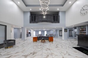 A spacious lobby with a marble floor, a central seating area, a staircase, and a clock on the wall. - Wingate by Wyndham Augusta/Fort Eisenhower (Augusta)