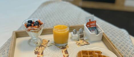 A breakfast tray with bacon, eggs, waffles, and a glass of orange juice on a bed.