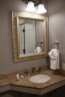 Un baño con un espejo grande y ornamentado, un lavamanos y dos anillos para toallas.
