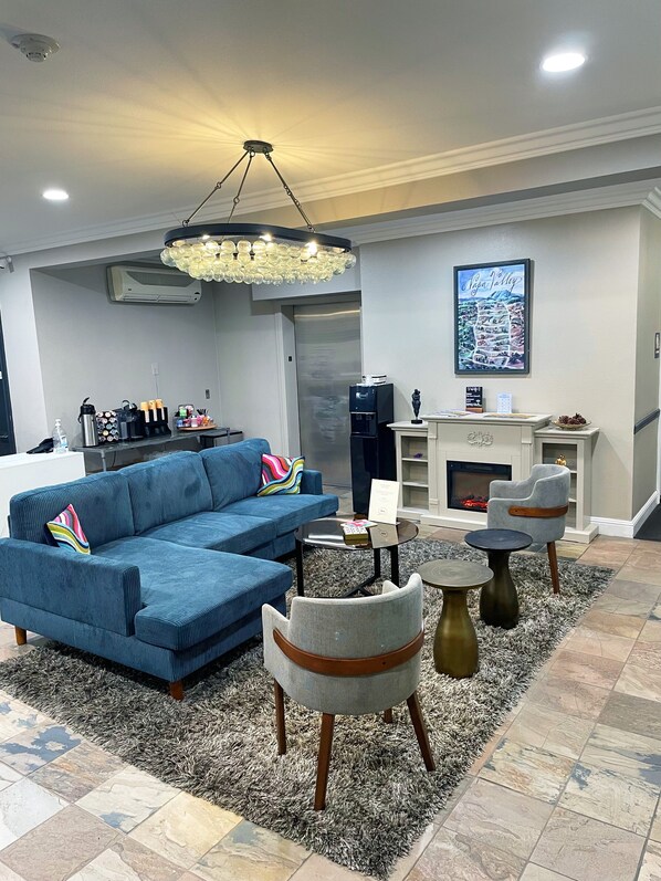 A modern living room with a blue sectional sofa, a grey armchair, and a round coffee table. There is a fireplace with a mantel and a framed picture above it.