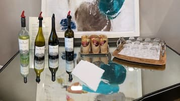 A table with wine bottles, glasses, and a tray of wrapped items, with a painting in the background.