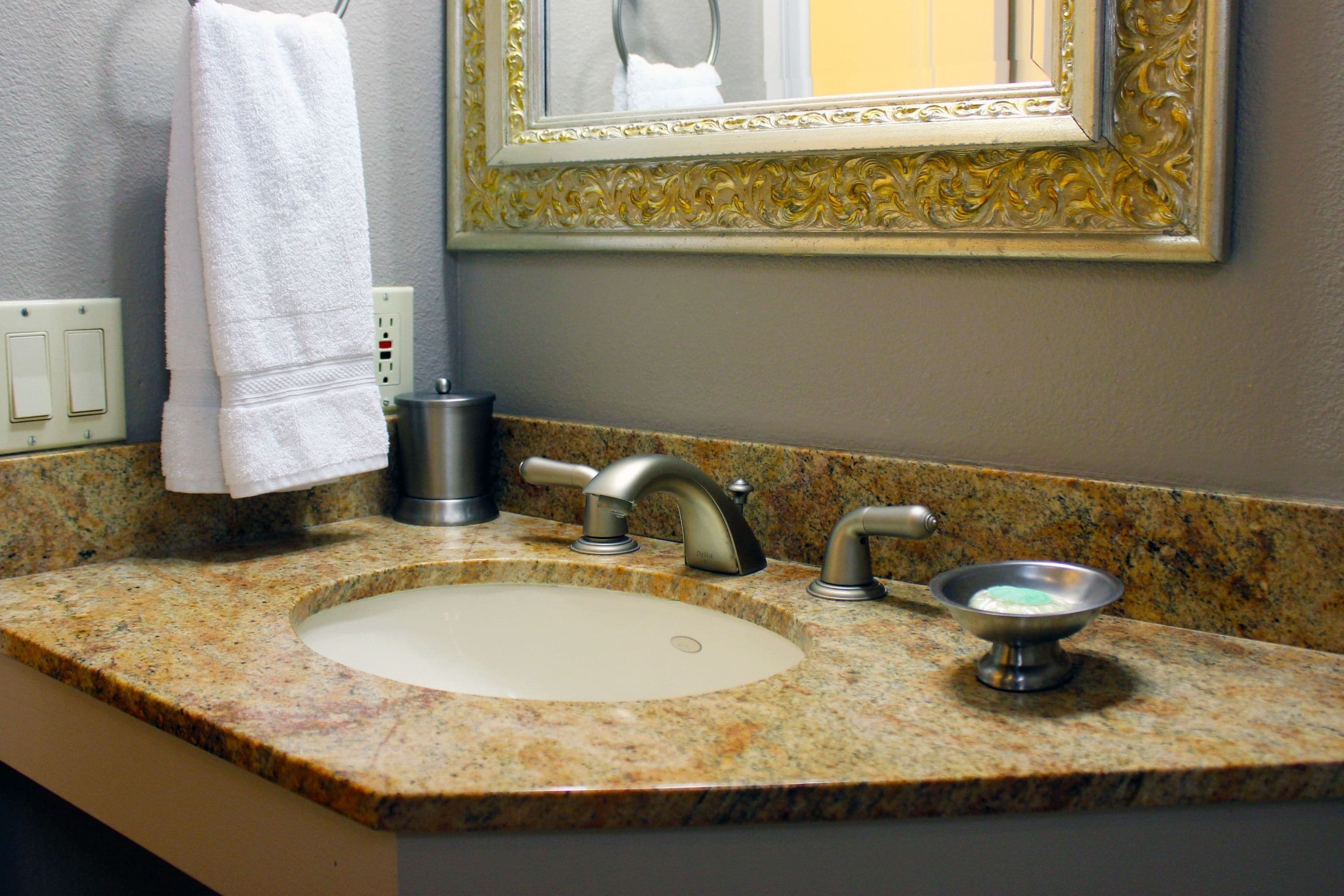 Un lavabo de salle de bain avec un plan de toilette en granit, un miroir doté d’un cadre orné et une serviette suspendue à un porte-serviettes.