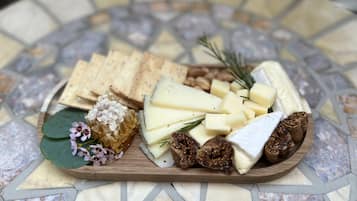 A wooden board with various cheeses, crackers, and nuts on a tiled table.