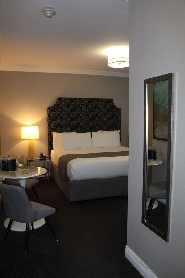 A hotel room with a bed, a desk with a lamp, a chair, and a painting on the wall.