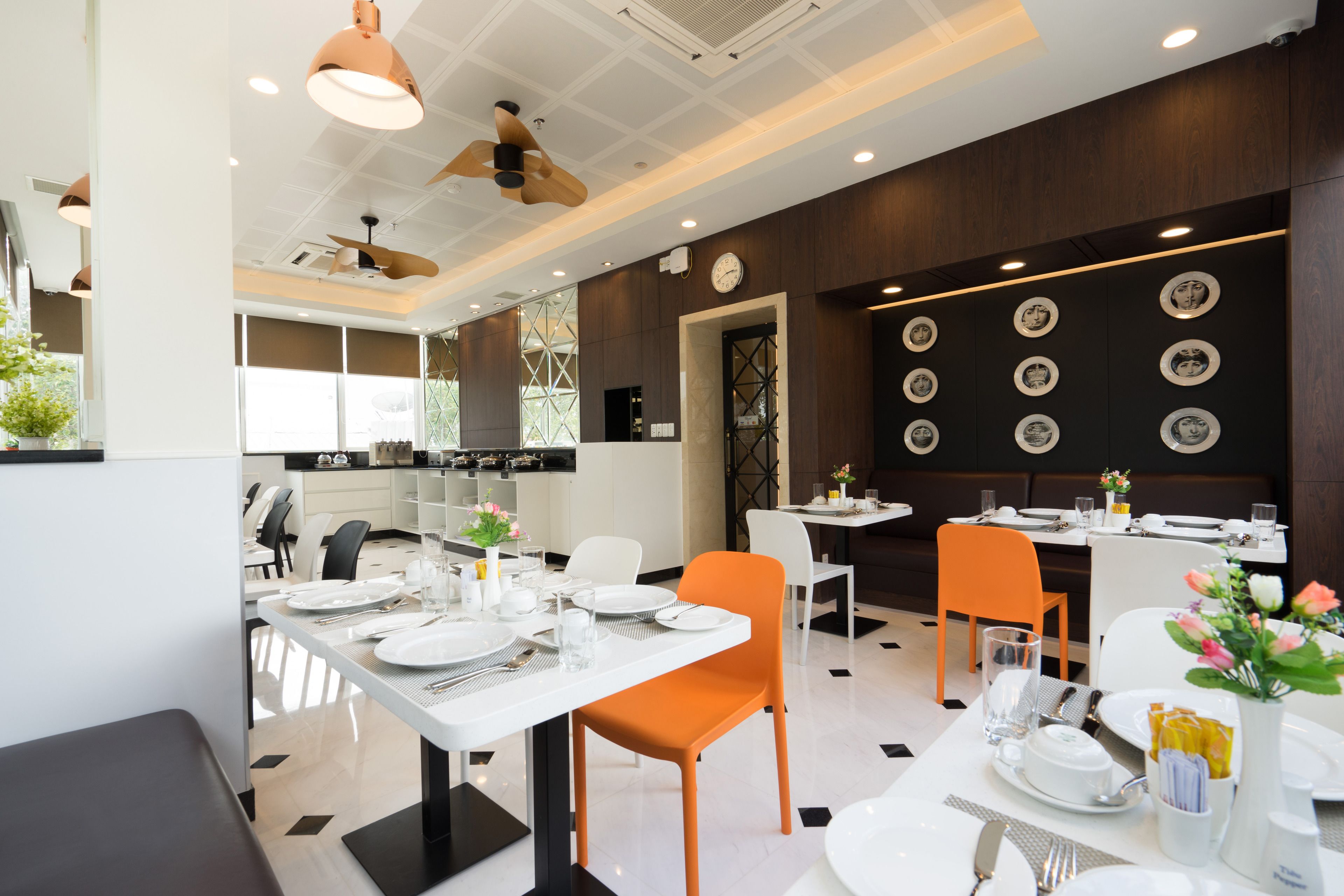 Un espace repas moderne avec des tables blanches, des chaises orange et un mur décoré d’assiettes rondes.