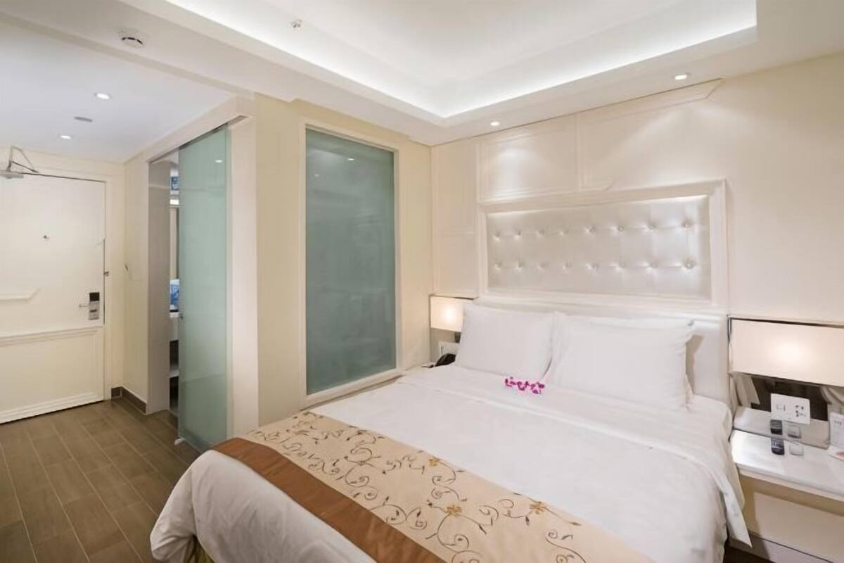 Ein Hotelzimmer mit einem großen Bett, Nachttischen, einem Kleiderschrank und einer Glastür zum Badezimmer.
