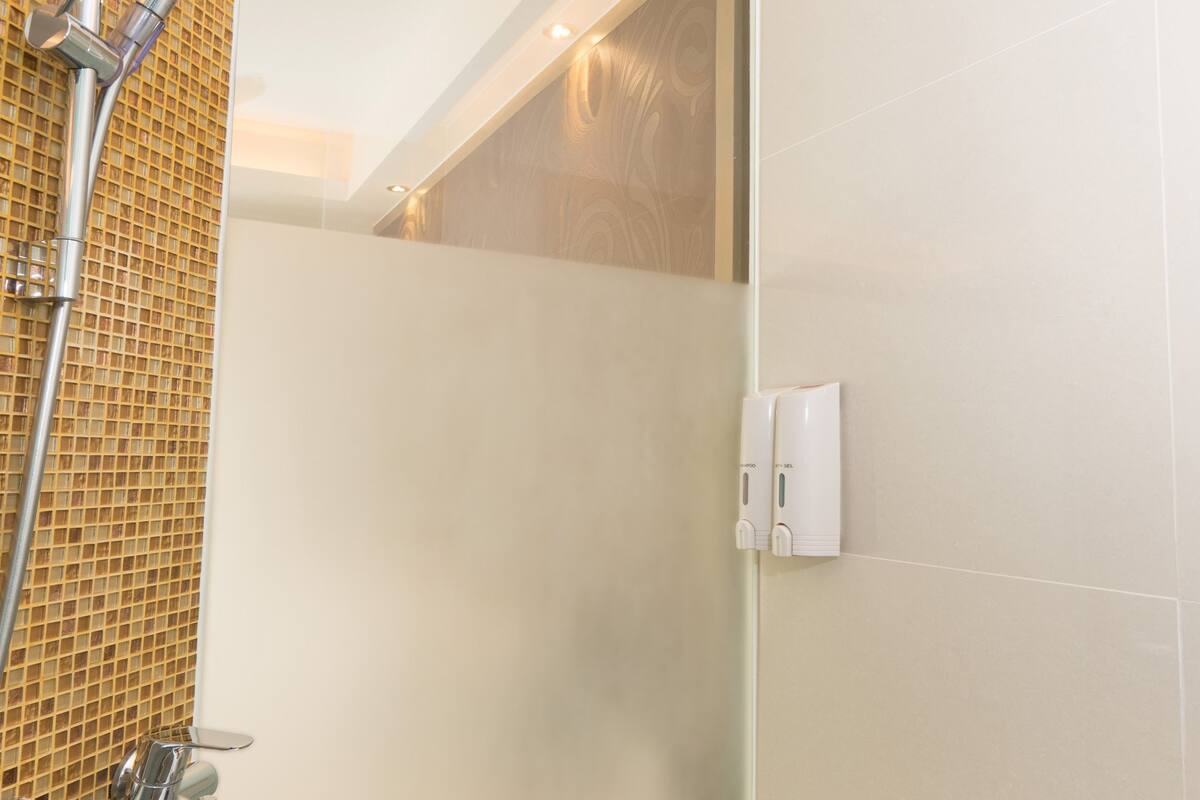 Ein modernes Badezimmer mit Duschkabine aus Glas, Handbrause und Wandseifenspender.
