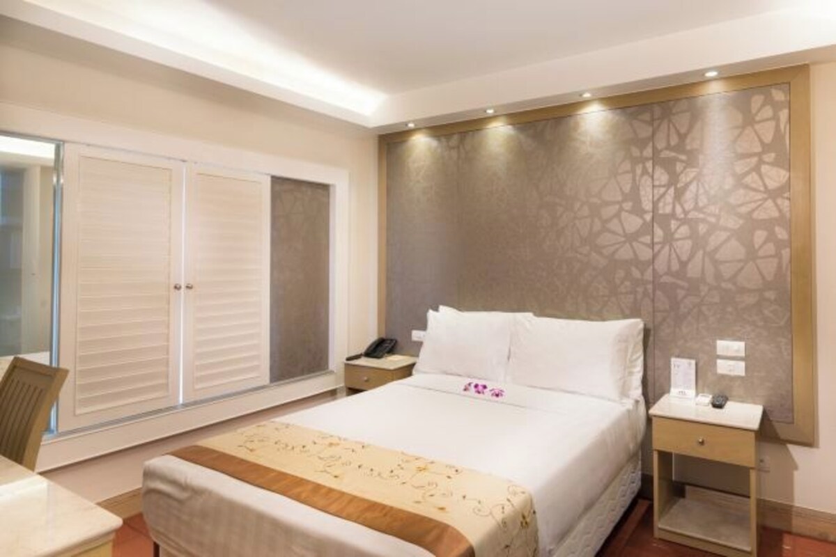 A hotel room with a bed, bedside tables, a desk, and a wardrobe.