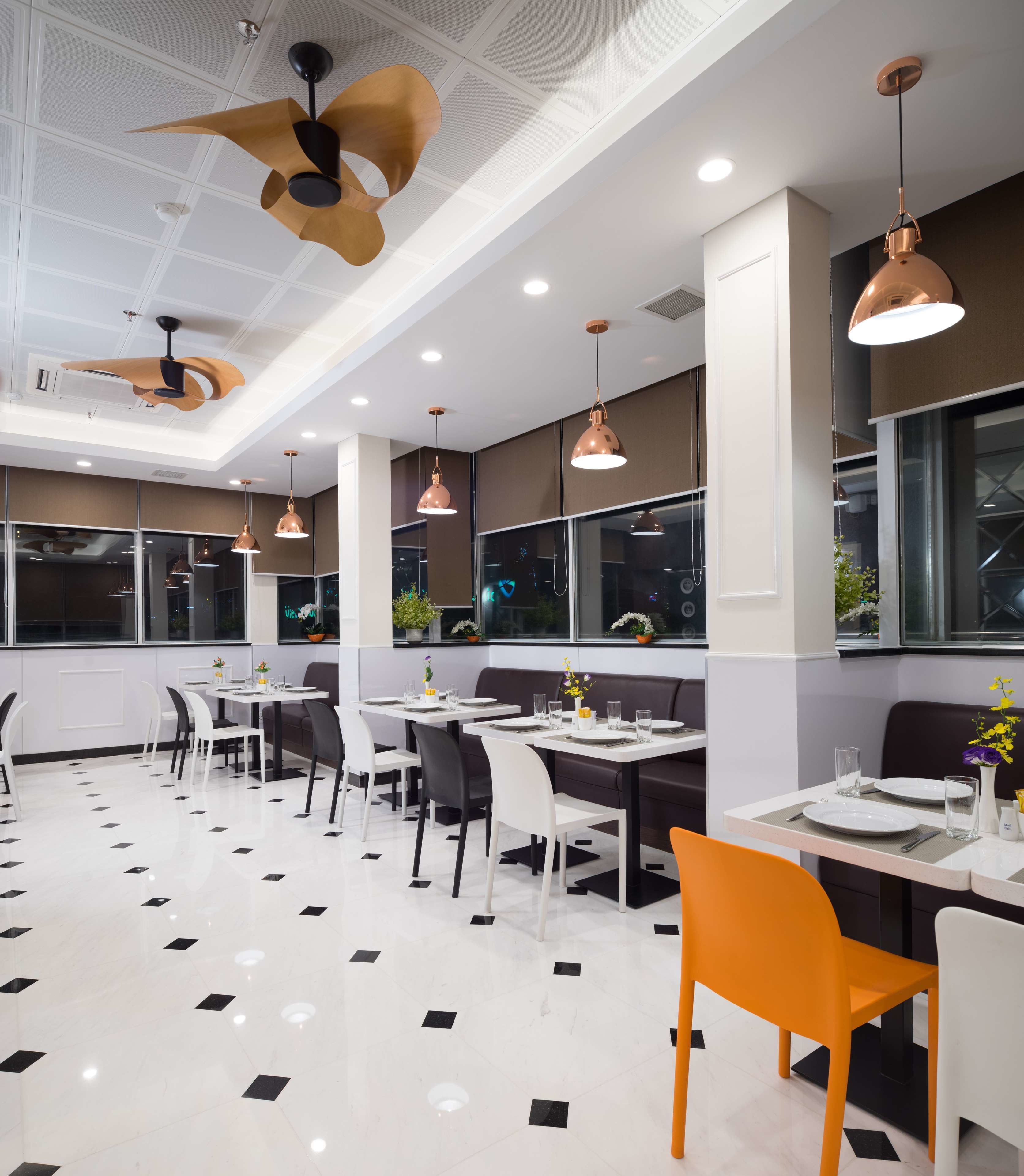 Un restaurant moderne avec un sol à carreaux noirs et blancs, de nombreuses tables à manger entourées de chaises et des luminaires suspendus.