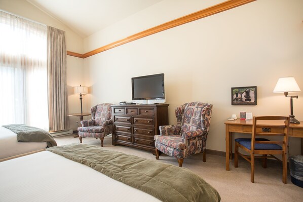 A hotel room with a bed, two armchairs, a desk with a chair, a television, and a lamp.