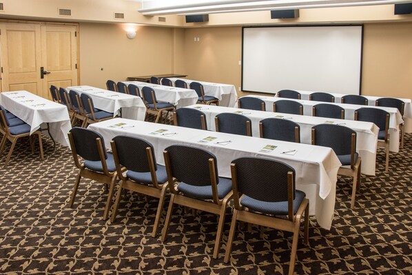 Una sala de conferencias con varias mesas y sillas, una pantalla de proyector y piso alfombrado.