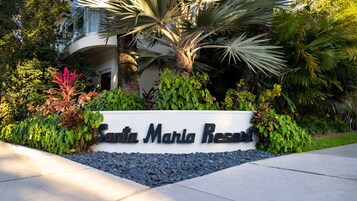 A sign for Santa Maria Resort surrounded by lush greenery and palm trees.