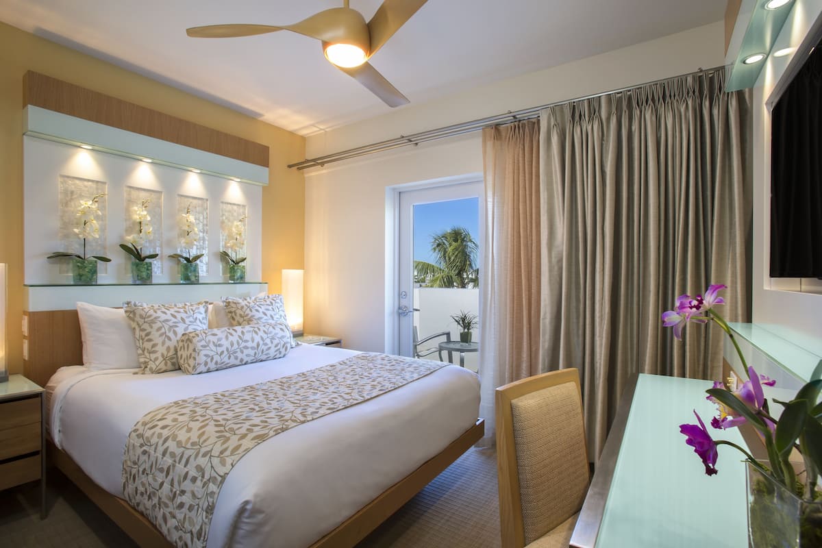 Quarto de hotel com cama, escrivaninha, cadeira, ventoinha no teto e vista para o exterior.