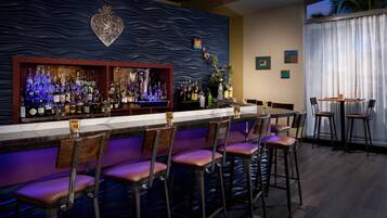 A bar area with a long counter, multiple stools, and a variety of bottles.
