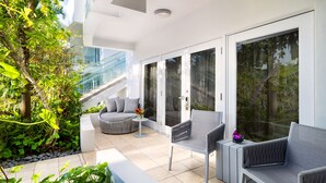 A modern outdoor seating area with a sofa, chairs, and a small table, surrounded by glass doors and a view of greenery. - Santa Maria Suites (Key West)