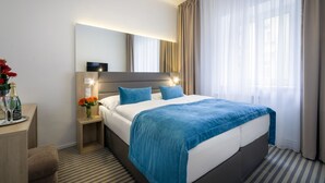 Habitación de hotel con cama, mesita de noche, lámpara y ventana con cortinas.