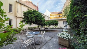 Un patio con una mesa redonda y sillas, rodeado de macetas con plantas y flores.