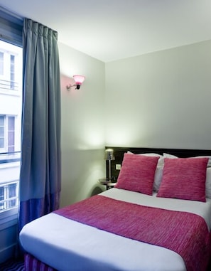 Une chambre d’hôtel avec un lit, une table de chevet, une lampe et une fenêtre avec des rideaux.