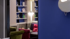 A modern interior with a blue accent wall, a seating area with a table, and shelves with decorative items. - Hôtel Antin Trinité (Paris)